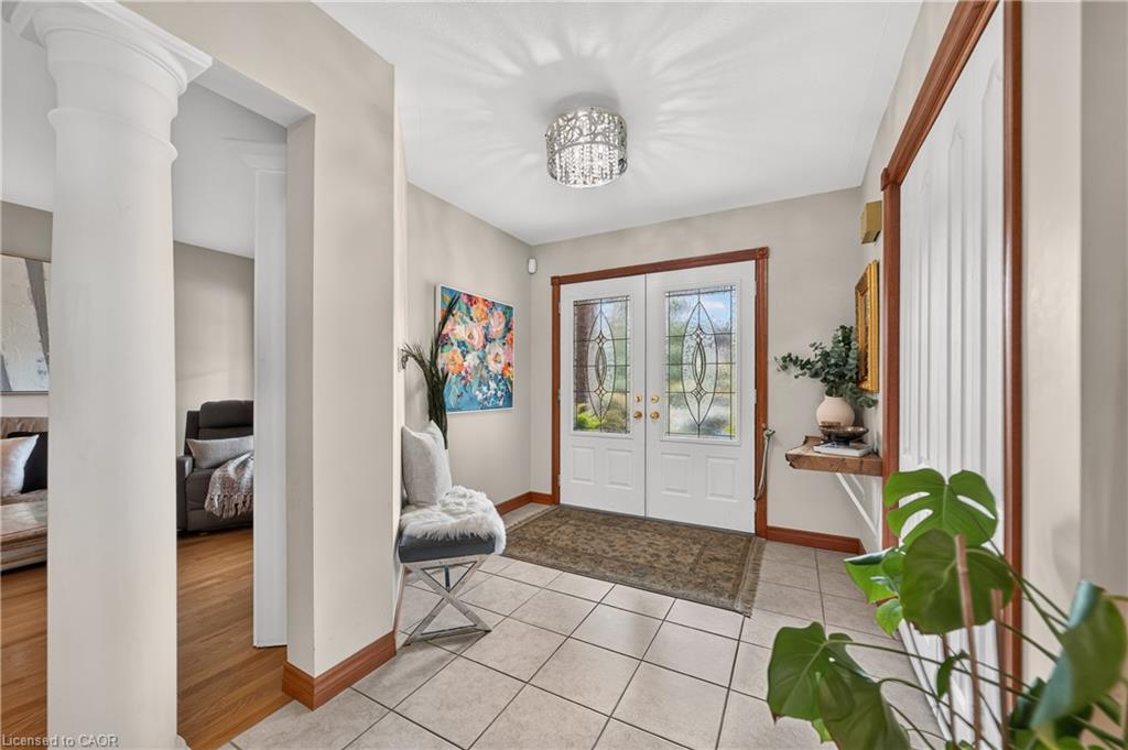 White double entry doors with leaded glass inserts, tiled flooring, decorative ceiling-mounted light fixture, and a structural column