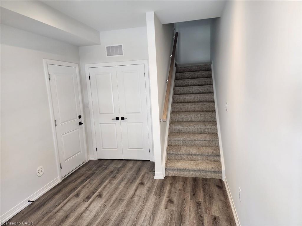 Wood-finish flooring, white paneled doors, matte black hardware, and carpeted stairs with a light wood handrail