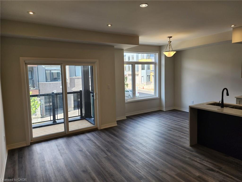 Spacious living area featuring wood-finish flooring, recessed lighting, and a sliding glass door opening to a private balcony with black metal railings