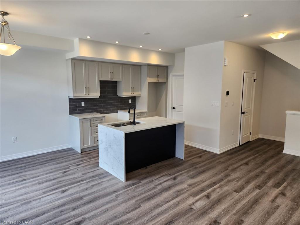 Contemporary kitchen island with a stone finish countertop and integrated sink, recessed lighting, wood-finish flooring, light cabinetry, and dark subway tile backsplash
