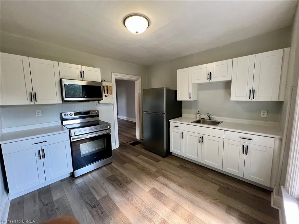 Modern kitchen featuring white shaker-style cabinetry, wood-finish flooring, stainless steel appliances, and light-toned countertops