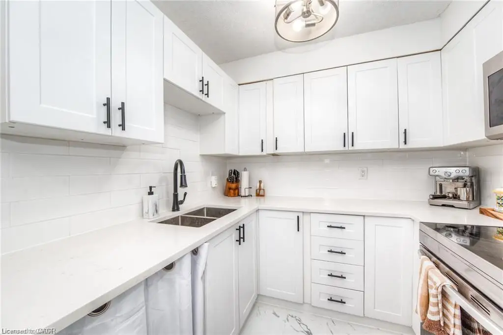 White shaker cabinetry with matte black hardware, dual basin stainless steel sink, black gooseneck faucet, light solid surface countertops, and white tile backsplash
