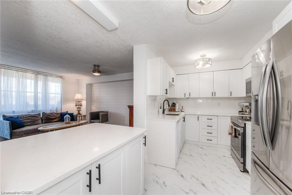 White shaker-style cabinetry with matte black hardware, stainless steel appliances, a white quartz countertop, and white marble-look flooring