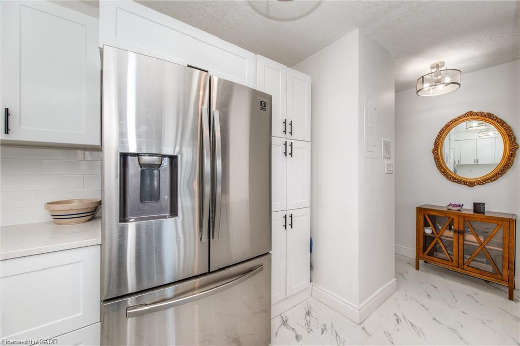 Stainless steel French door refrigerator with integrated ice and water dispenser, white shaker-style cabinetry, subway tile backsplash, light-toned countertop, and marble-look flooring