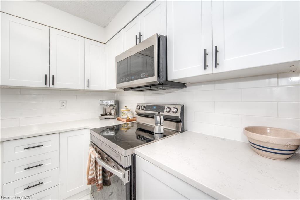 White cabinetry with black hardware, white subway tile backsplash, light-toned countertops, and stainless steel appliances