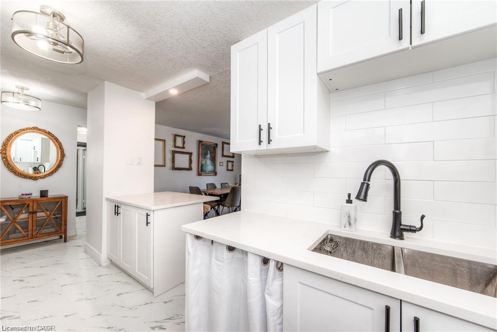White shaker-style cabinetry, white countertops, stainless steel double basin sink, matte black faucet, and white subway tile backsplash