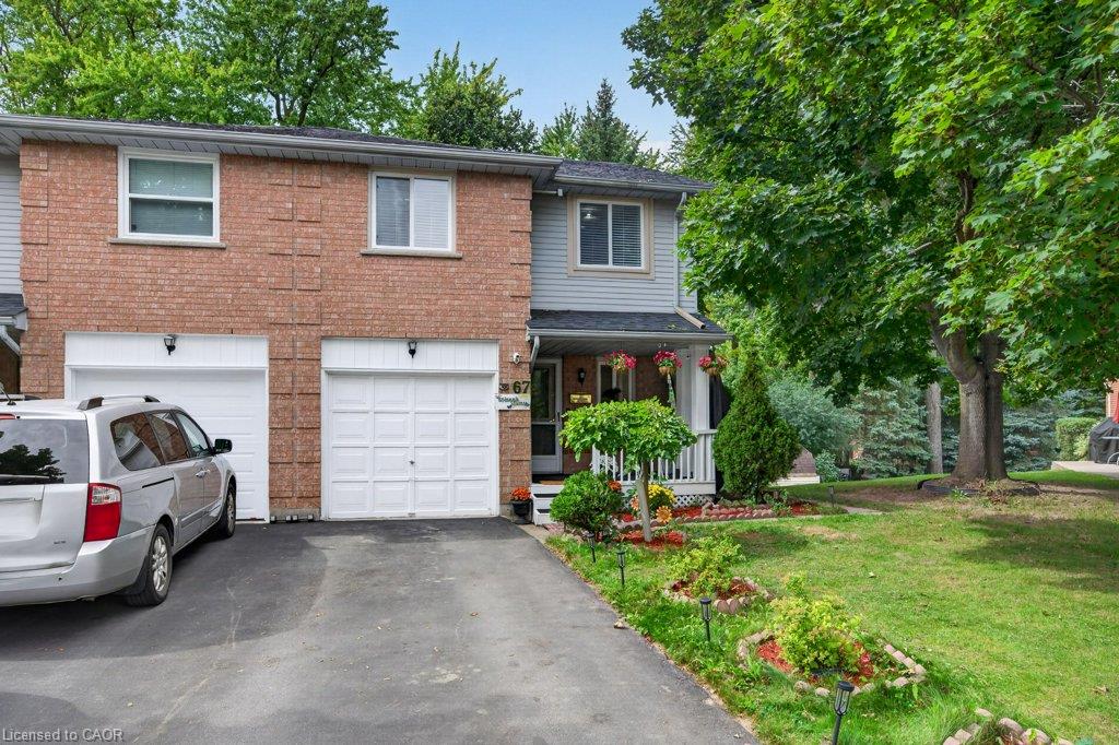 Brick exterior with white garage doors, asphalt driveway, front porch with white railing, and mature trees