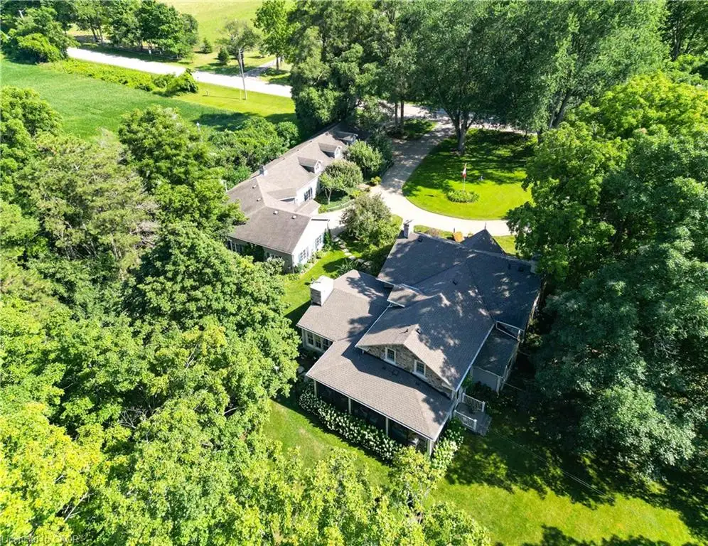Expansive property featuring multiple structures with dark shingle roofs, surrounded by mature trees and manicured green spaces