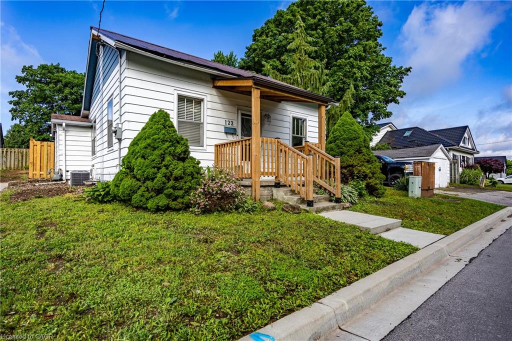 White siding exterior with a dark metal roof, featuring a covered porch with natural wood railings and steps