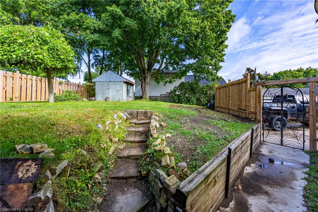 backyard featuring a wood retaining wall, stone steps, and a wrought iron gate