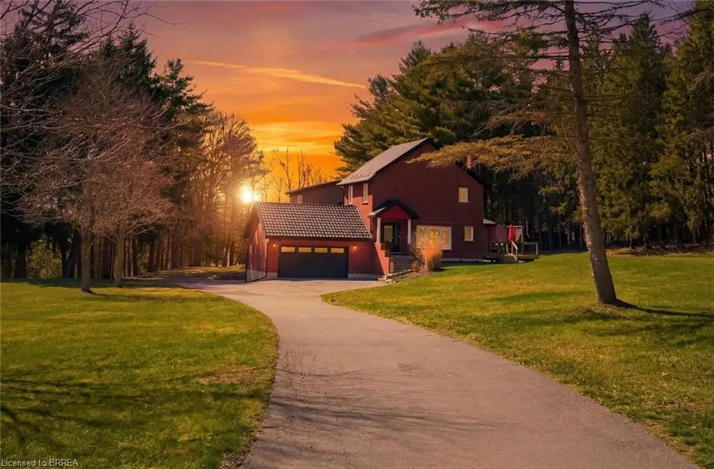 View of front of house with a tiled roof, a front lawn, driveway, a garage, and view of wooded area