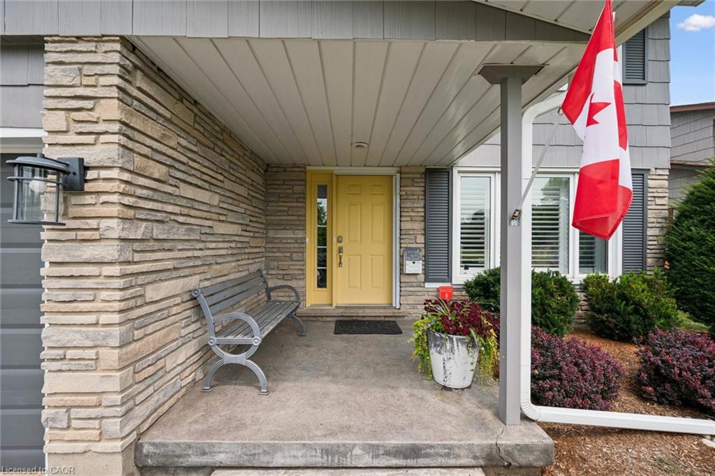 Covered concrete front porch featuring a yellow entry door with sidelight, stone veneer siding, and a decorative wall-mounted light fixture