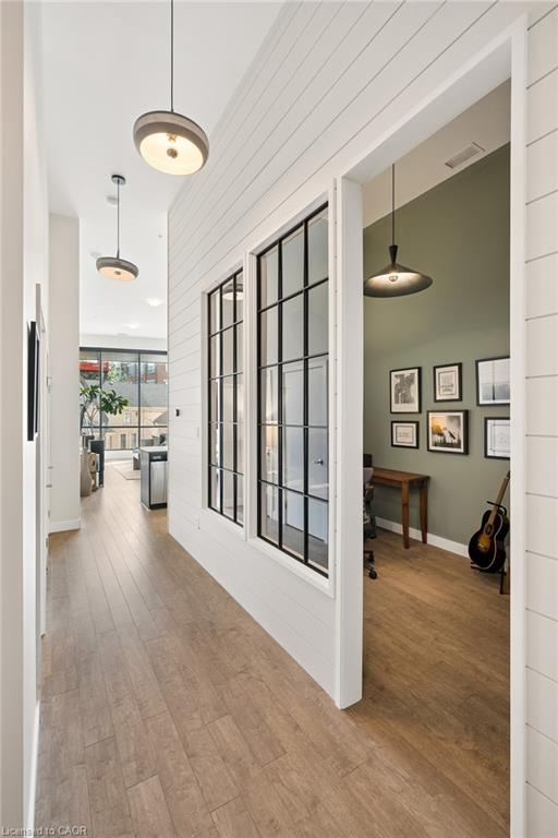Hallway with wood-finish flooring, shiplap accent wall, and contemporary pendant lighting