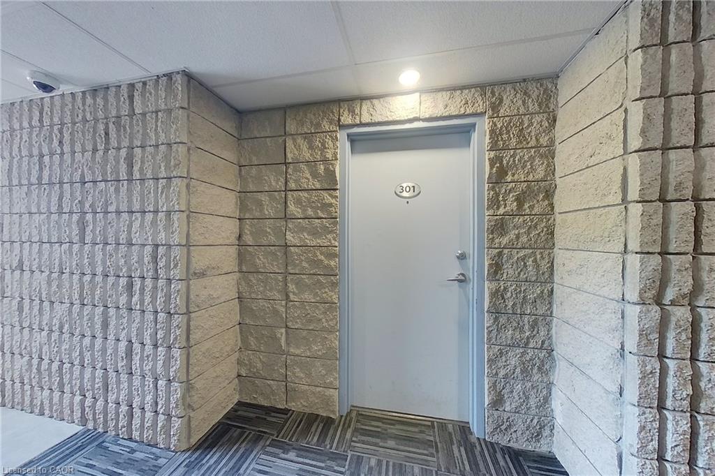 Entryway featuring textured block walls, a light gray door with a prominent unit number, recessed ceiling lighting, and patterned floor tiling