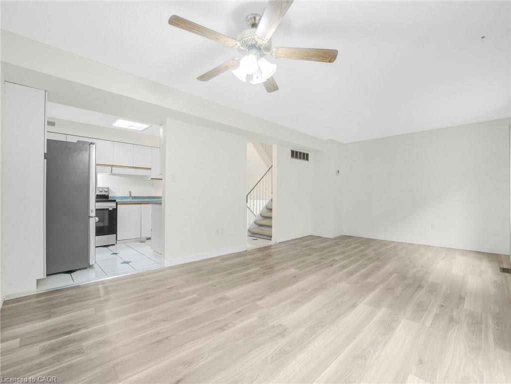 Open-concept living space featuring wood-finish flooring, a ceiling fan, and a kitchen with white cabinetry and stainless steel appliances