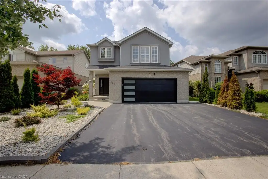 Two-story stucco and brick exterior featuring a black garage door with frosted glass panels, a paved driveway, and a landscaped front yard with varied plantings