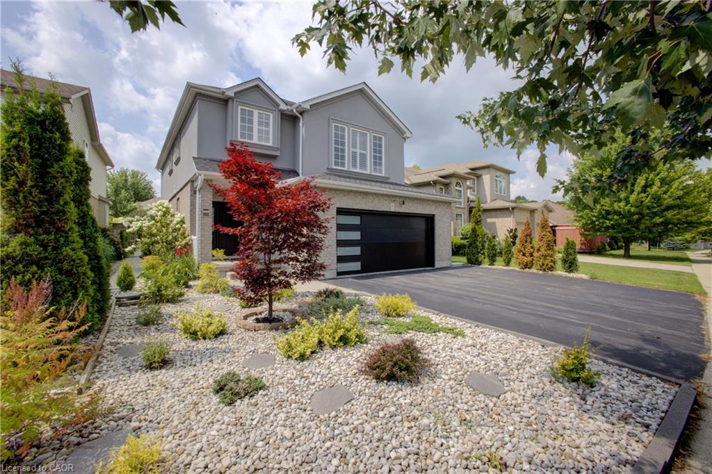 Contemporary architecture with a two-car garage featuring a modern door, a paved driveway, and a rock garden with mature plantings