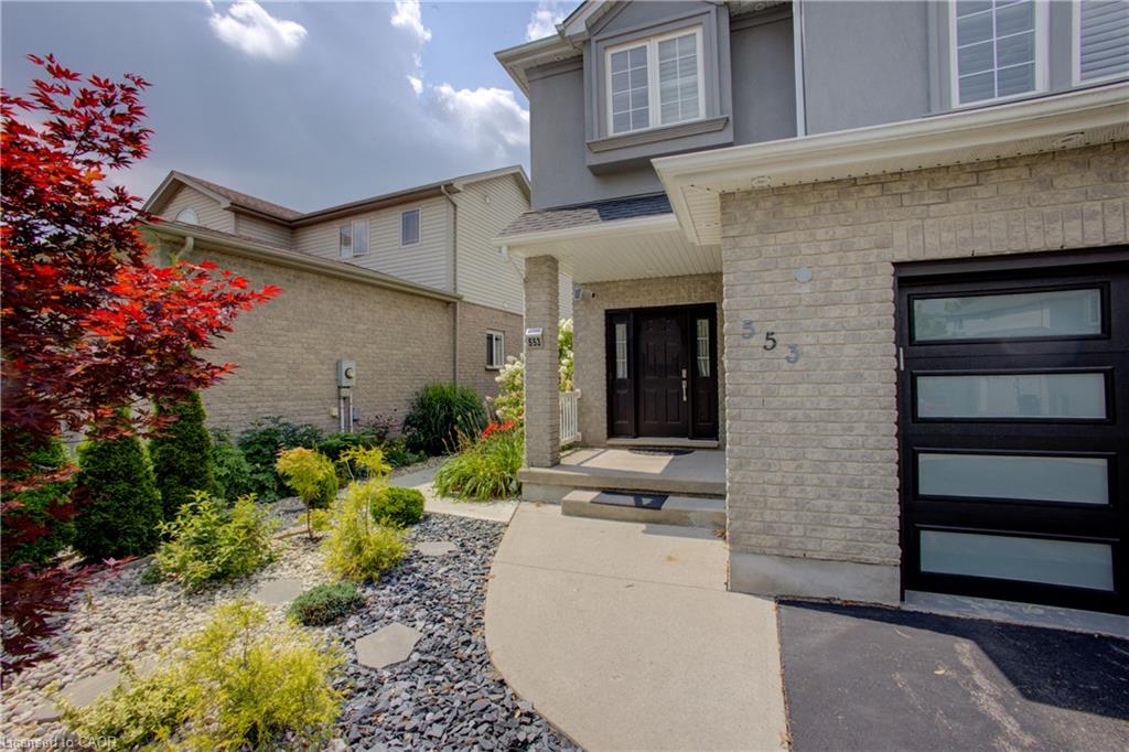Brick exterior with stucco accents, modern garage door with frosted glass panels, double entry doors, covered porch, and landscaped front yard with varied plantings