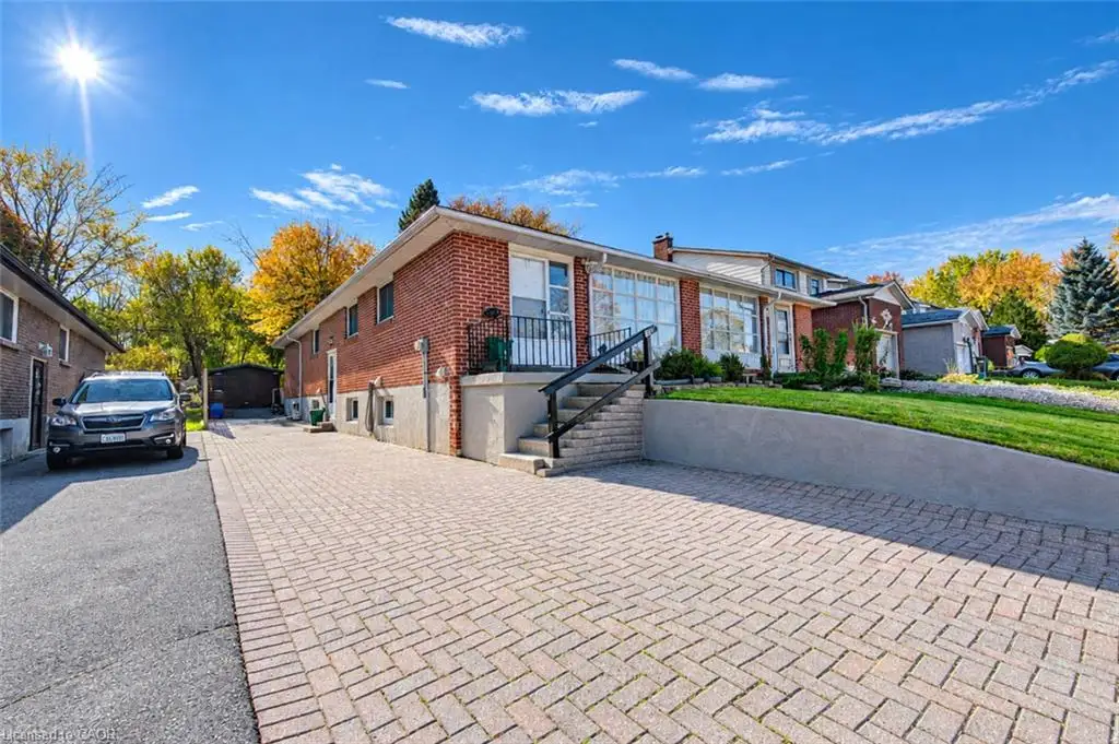 Brick exterior featuring a herringbone-patterned paver driveway, raised concrete retaining wall, and exterior staircase with metal railing
