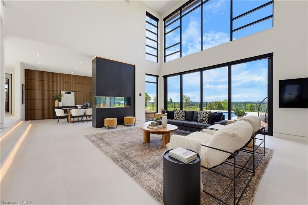 Soaring ceilings, expansive window walls, sleek built-in fireplace, wood-finish accent wall, and light-toned flooring