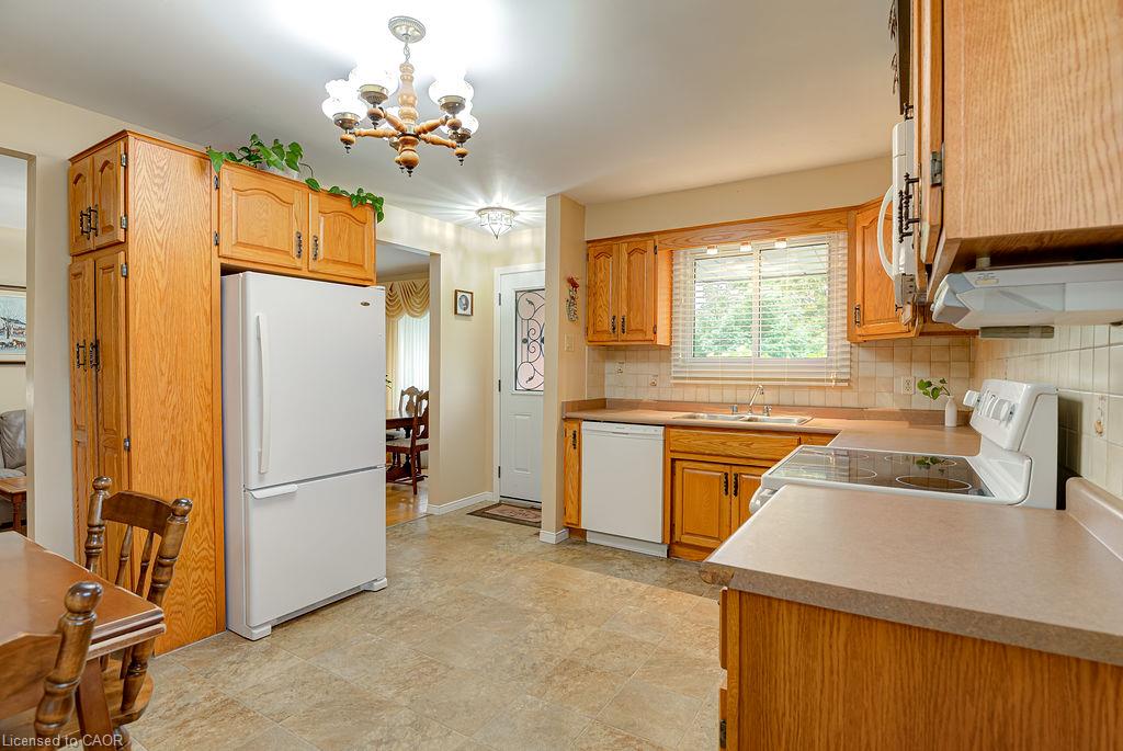 Wood-finish cabinetry and trim, neutral countertops, tile flooring, and white appliances including a refrigerator, dishwasher, and electric range