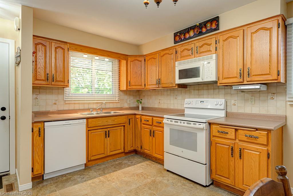 Kitchen featuring wood-finish cabinetry, built-in microwave, white electric range, and a double-basin sink