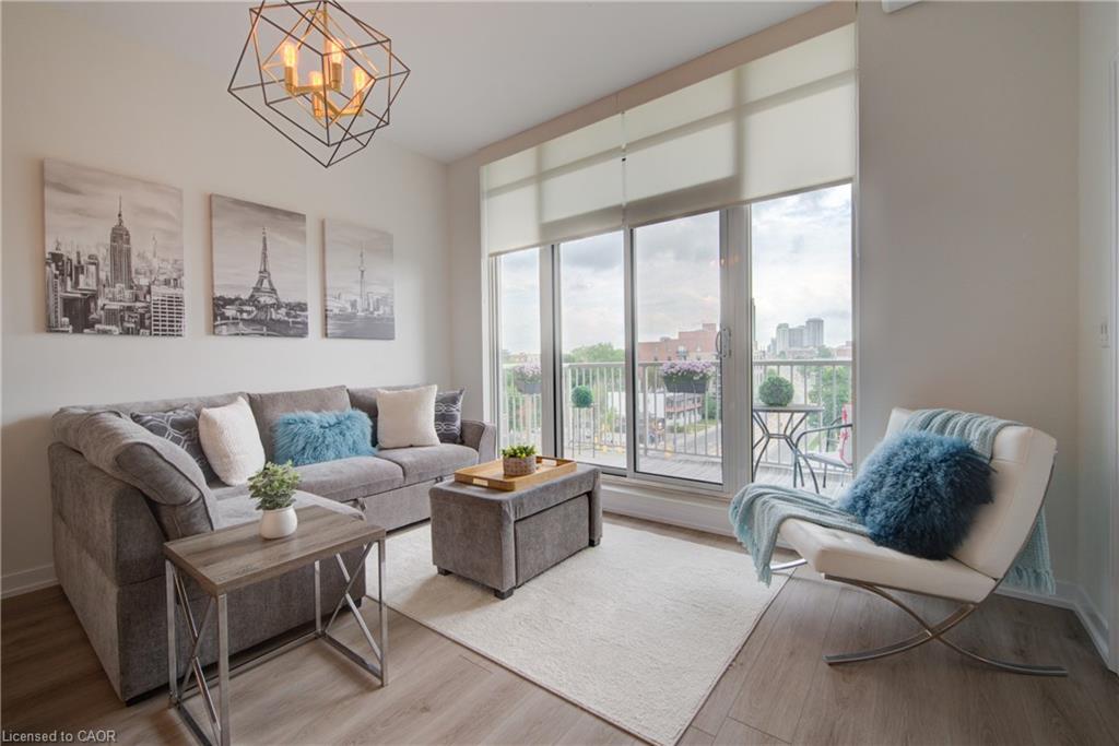 Living space featuring wood-finish flooring, a contemporary geometric chandelier, and full-height windows with roller shades