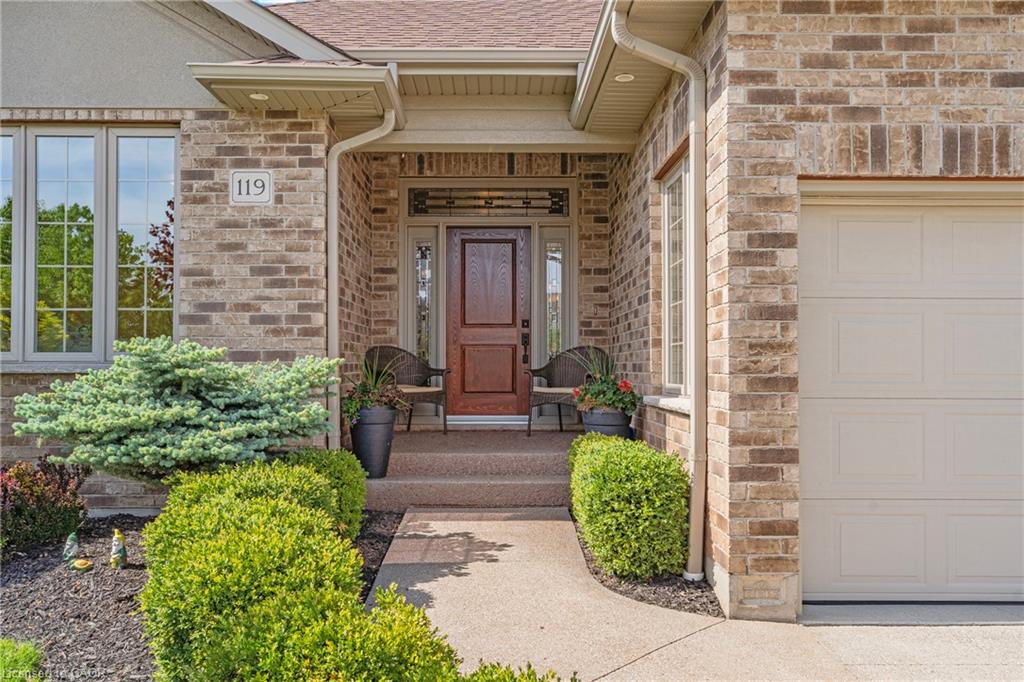 Brick exterior with a prominent entry door and decorative sidelights, featuring a paved walkway, established landscaping, and an integrated garage