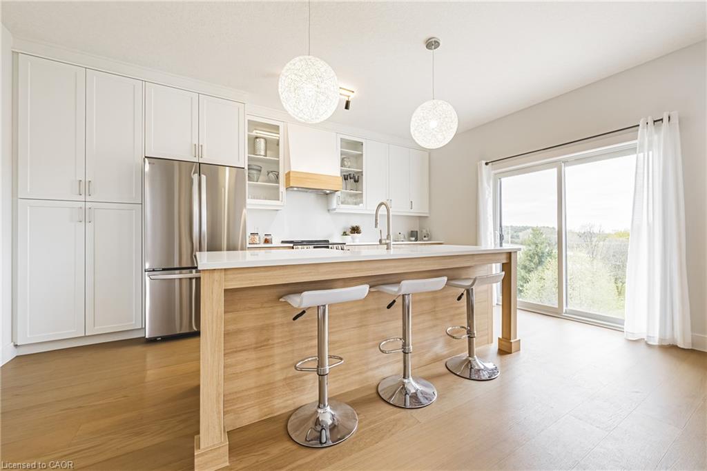 Contemporary kitchen featuring white cabinetry, stainless steel appliances, a center island with countertop seating, wood-finish flooring, and a sliding glass door