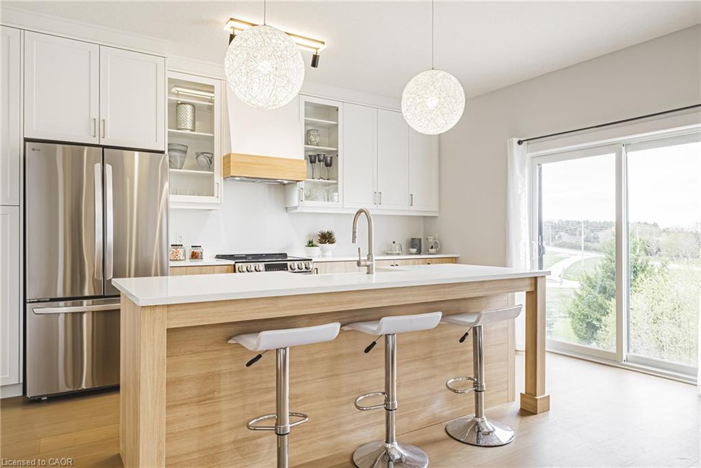 Kitchen featuring white cabinetry, stainless steel appliances, a center island with a light-toned countertop, wood-finish flooring, and sliding glass doors