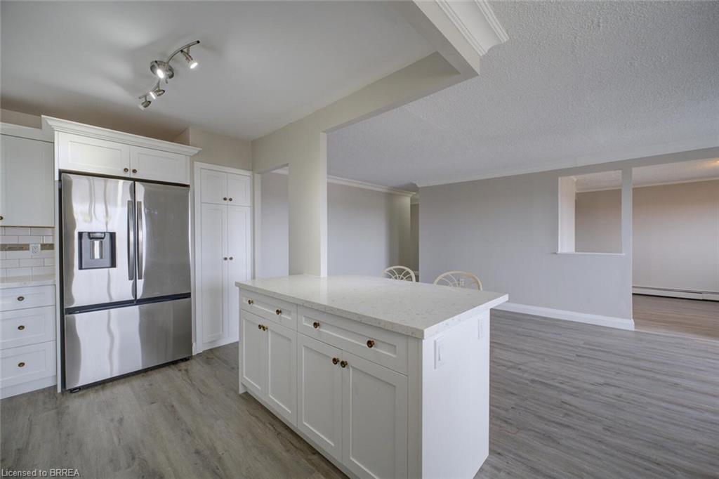 Kitchen featuring a central island with a light-toned countertop, white cabinetry with dark hardware, stainless steel refrigerator, and wood-finish flooring