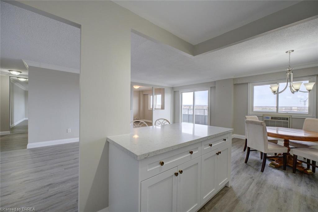 Open-concept living area featuring light wood-finish flooring, a white kitchen island with a light-toned countertop and cabinet storage, and a dining area with a chandelier