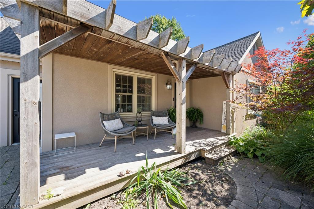 Exterior featuring a wood-beam pergola, wood-deck patio, stucco siding, multi-pane windows, and a stone pathway