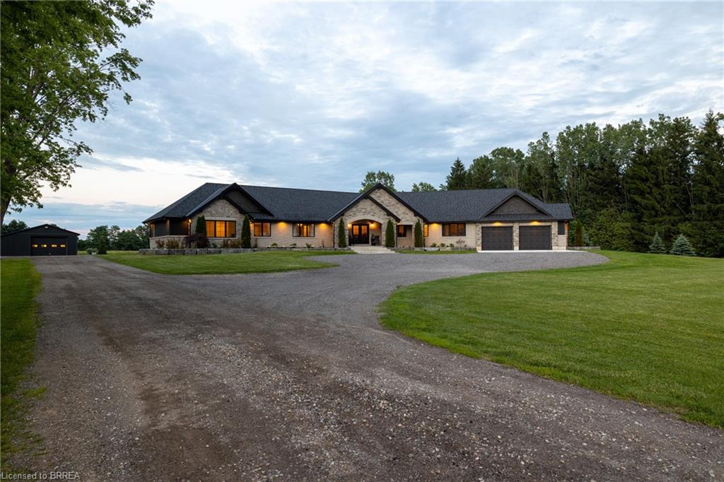 Stone and stucco exterior with a dark shingle roof, featuring a two-car attached garage, a separate detached garage, and a gravel driveway