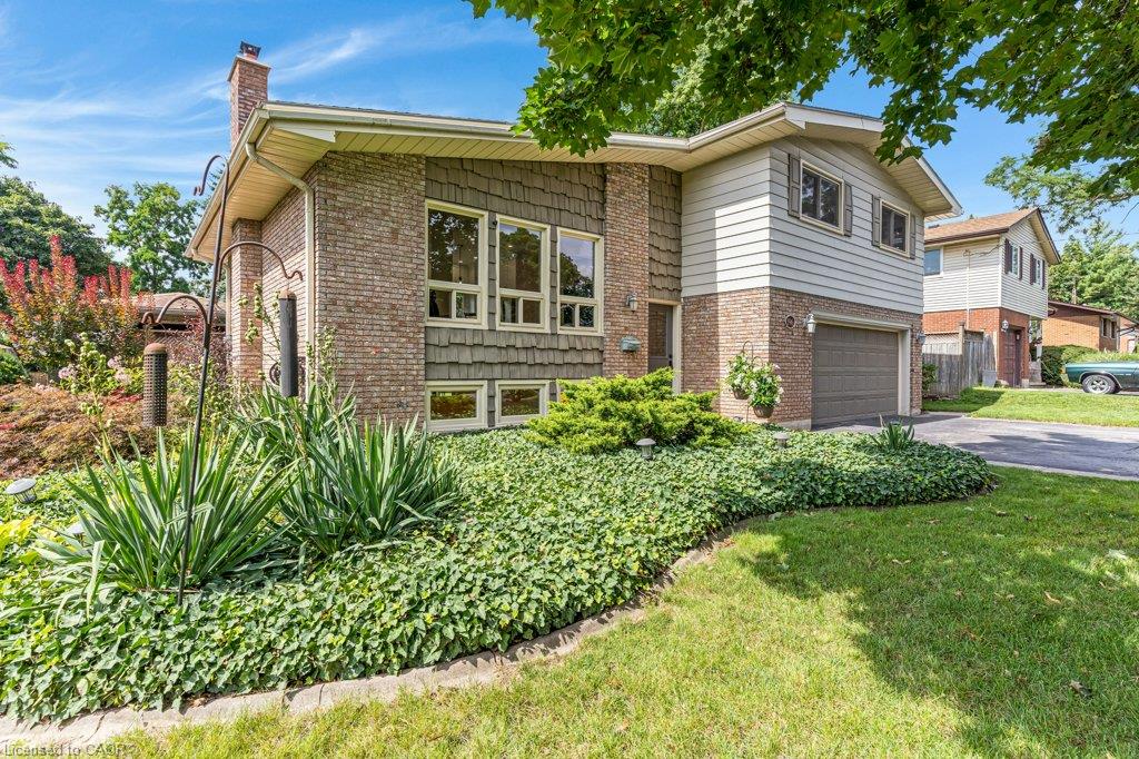 Brick exterior with white siding and decorative shingles, multiple large windows, attached garage, and a lush, landscaped front yard with ground cover