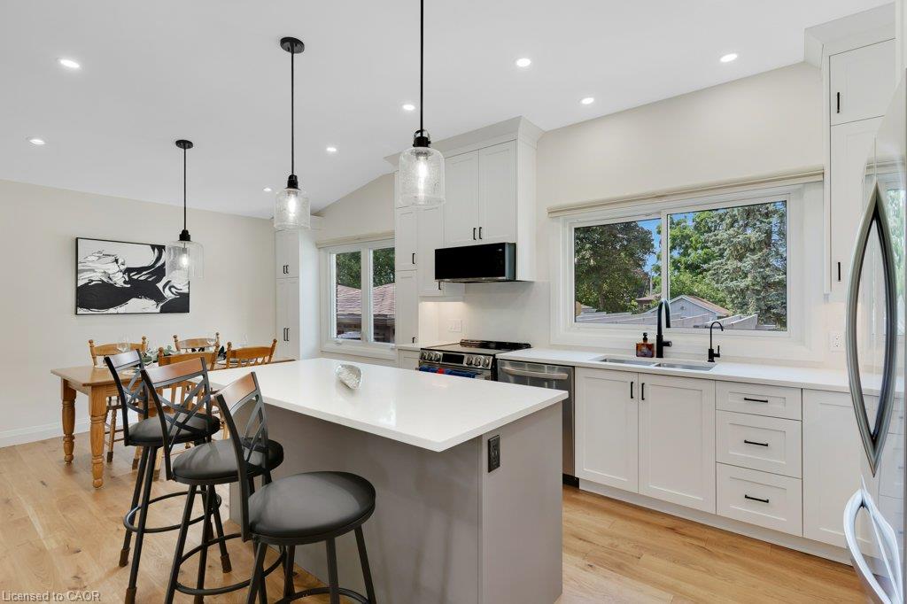 Open-concept kitchen featuring an eat-at island with a light-toned countertop, white cabinetry with black hardware, stainless steel appliances, and wood-finish flooring
