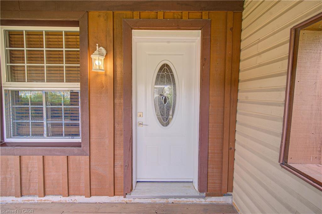 White entry door with an oval-shaped decorative glass insert, flanked by wood-paneled siding and a grid-pattern window
