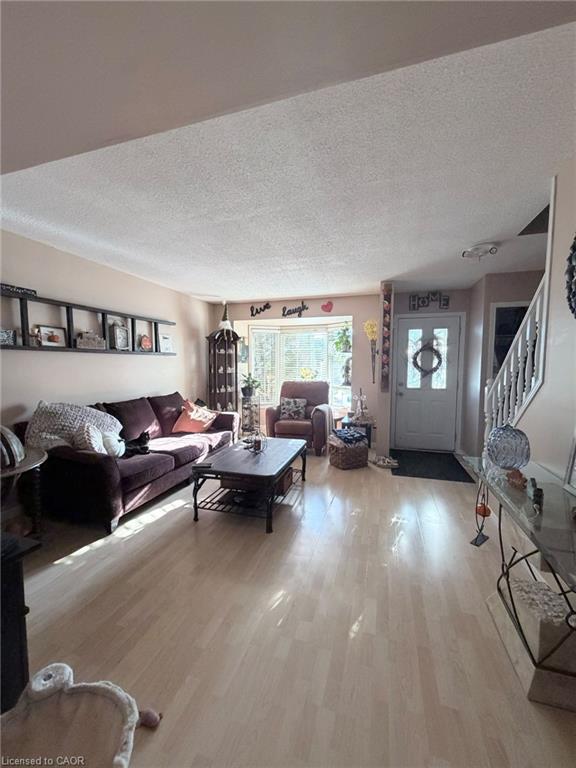 Light wood-finish flooring, bay window, white paneled entrance door, and a white staircase with dark handrails