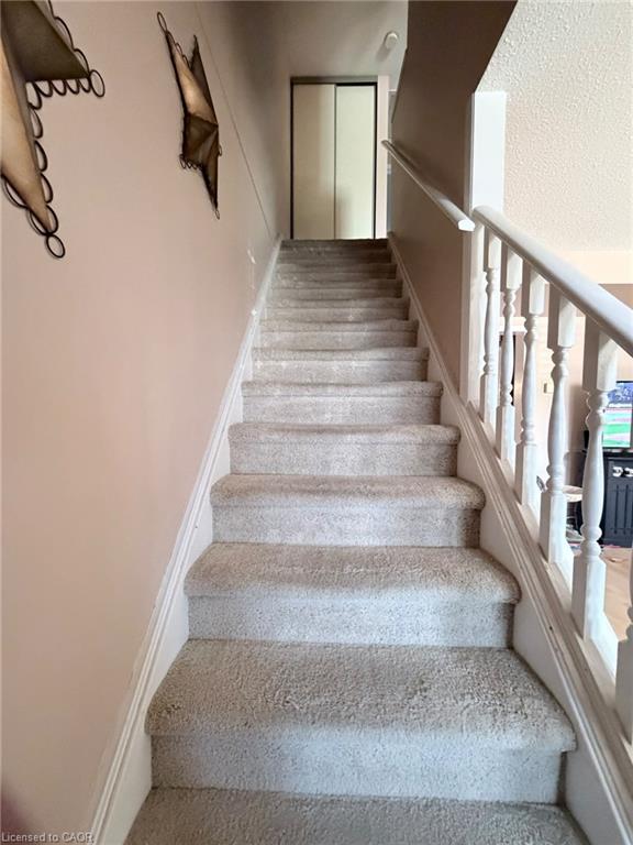 Carpeted staircase with painted wooden balusters and handrail leading to an upper landing with a closet featuring sliding panel doors