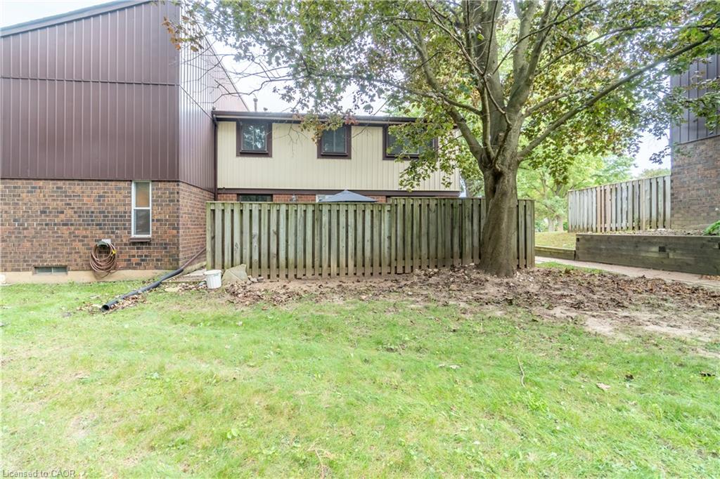Brick and siding exterior with a wood fence, mature tree, and green lawn