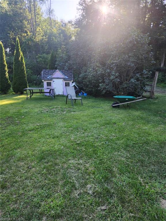 Expansive backyard oasis featuring a manicured lawn, mature tree-lined perimeter, and charming detached garden structure with covered porch