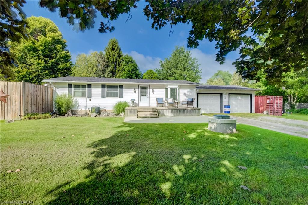 White siding exterior with black shutters, concrete front patio, attached two-car garage, gravel driveway, and a wooden privacy fence