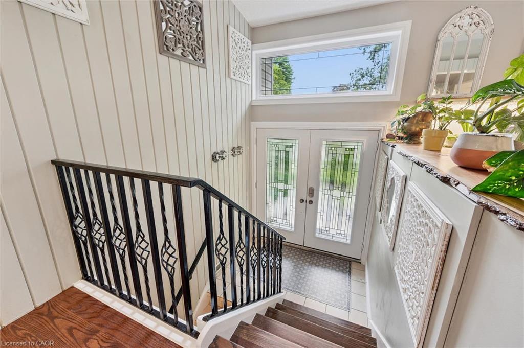 Wood-finish flooring, white paneled wall, wrought iron staircase railing, double entry doors with decorative glass, and a large transom window