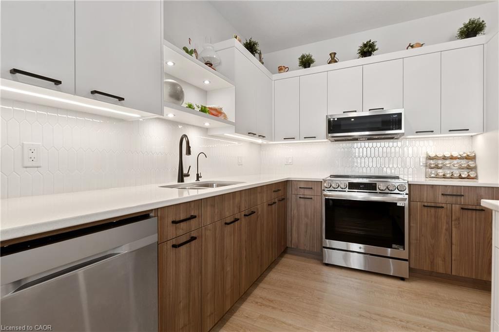 Contemporary kitchen featuring two-tone cabinetry, white countertops, a mosaic tile backsplash, and stainless steel appliances