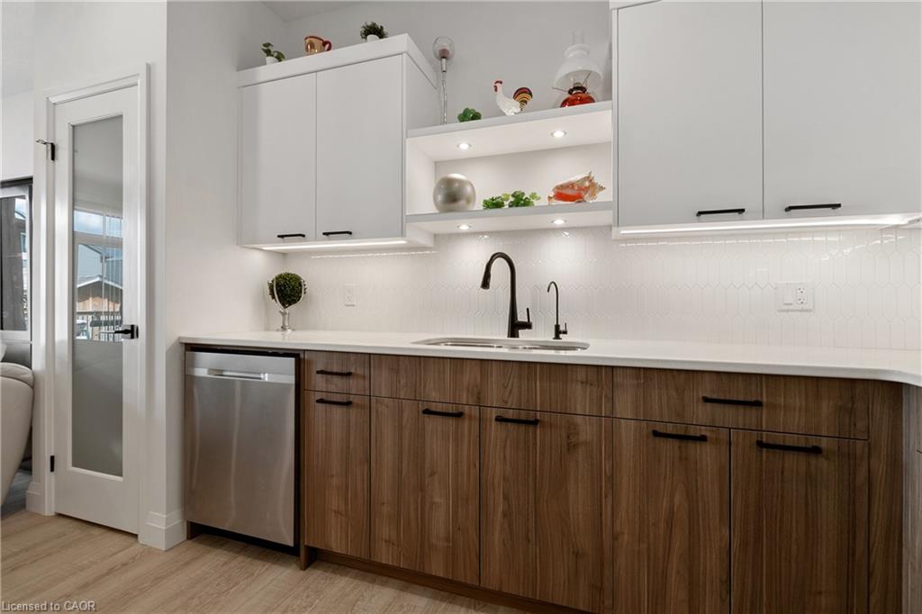 Contemporary kitchen featuring a stainless steel dishwasher, wood-finish lower cabinetry, white upper cabinetry, and contrasting matte black hardware