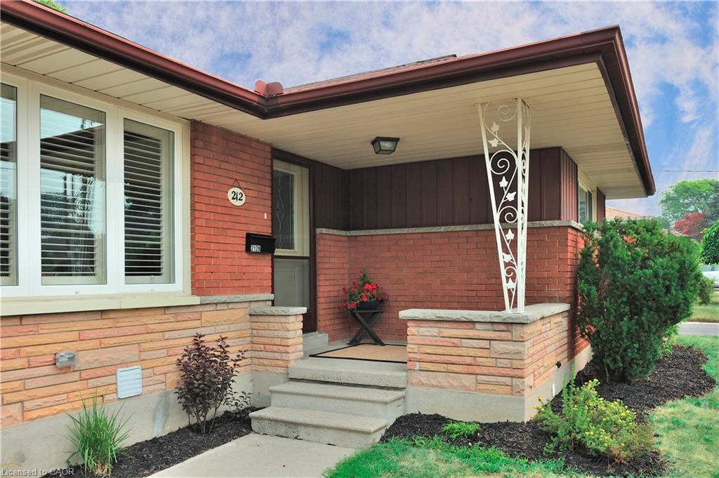 Brick facade with stone veneer accents, concrete steps, wrought iron porch column, and a covered entry