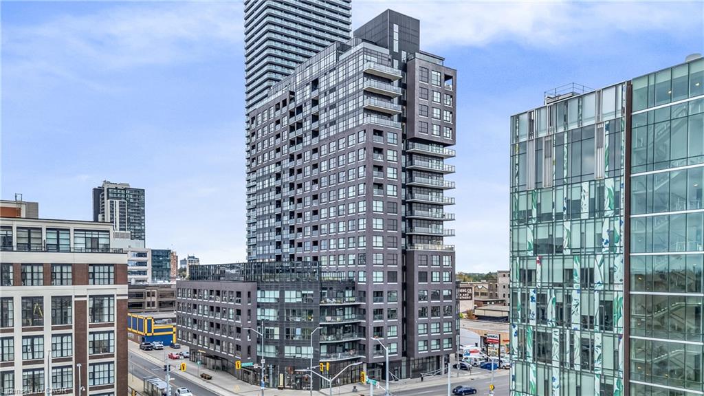 Modern high-rise building with a dark grey facade, multiple levels of balconies, a glass and metal exterior, and a prominent rooftop architectural feature