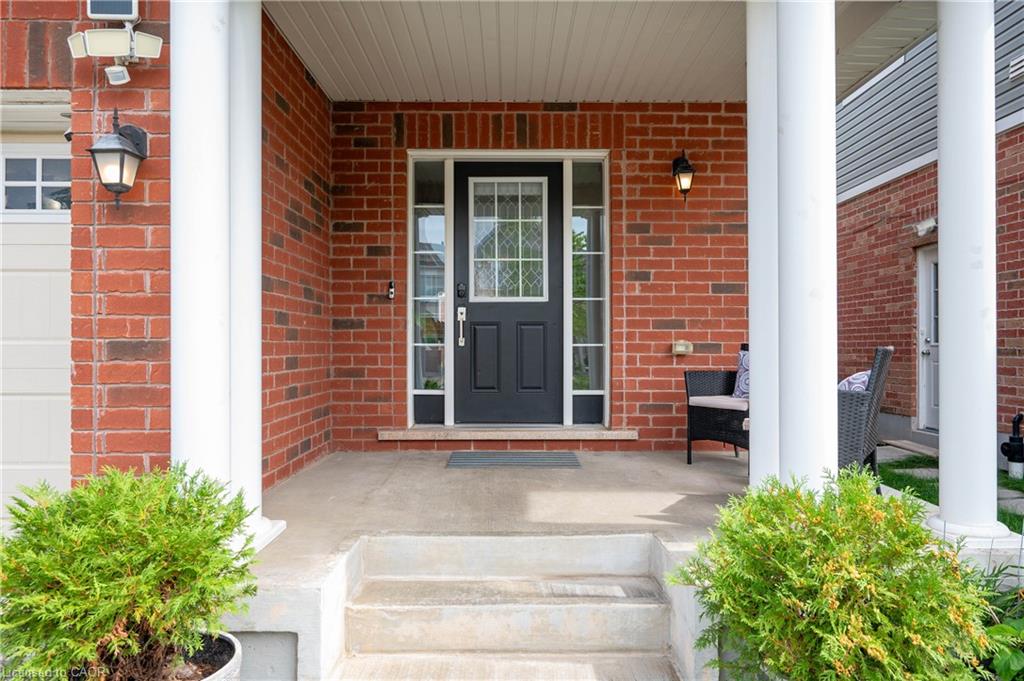 Brick exterior with a covered porch, featuring white support columns, a dark panel door with decorative glass, and a concrete entry pad with steps