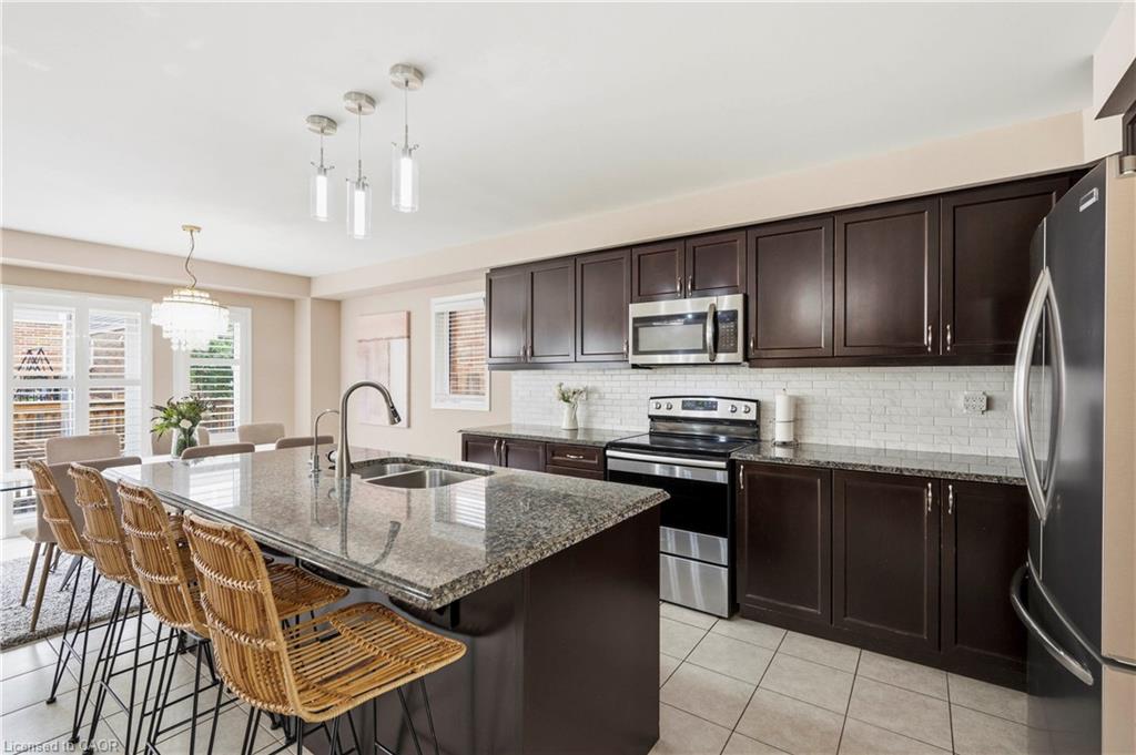 Kitchen featuring dark wood-finish cabinetry, stainless steel appliances, a tile backsplash, and a large island with a stone countertop