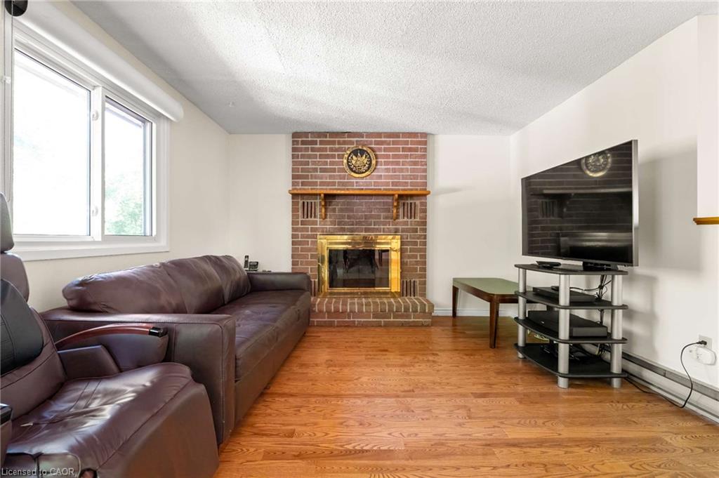 Hardwood-finish flooring, brick-surround fireplace with wood mantel, large window, and white walls